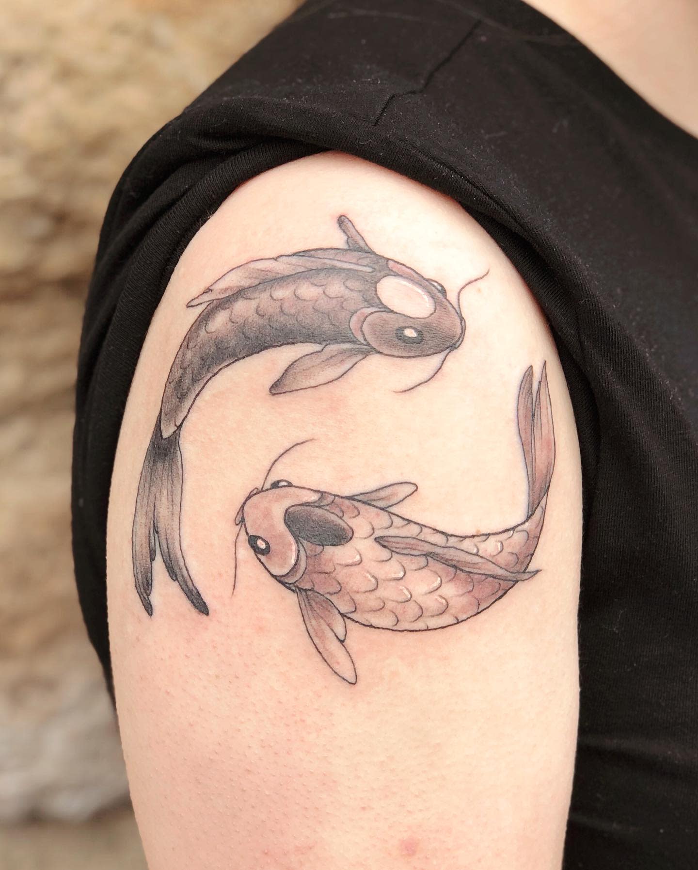 Tattoo of two koi fish swimming in a circular pattern on an upper arm